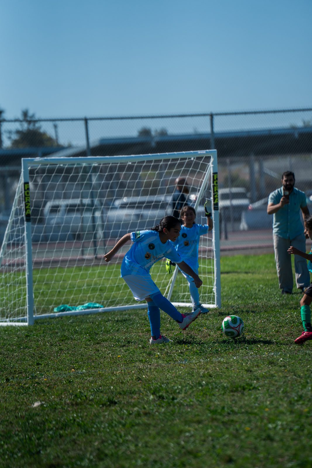 A goalkeeper in light blue stretching across the goalmouth