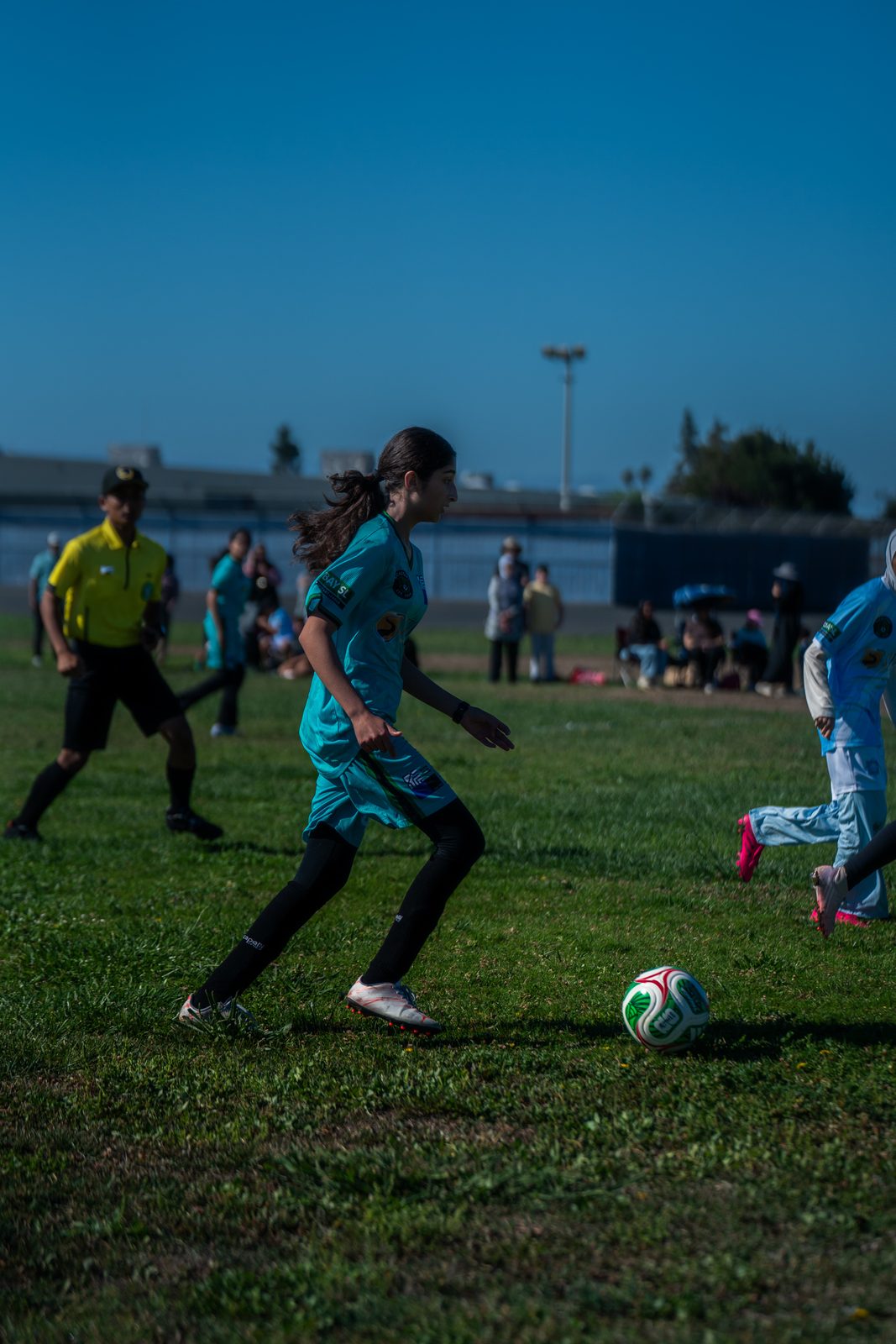 A player in teal carrying the ball upfield past the referee